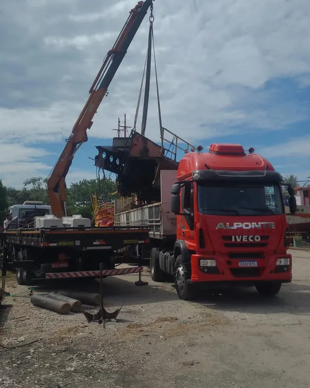 Caminhão da Alponte ao lado de guindaste içando uma estrutura metálica de balsa